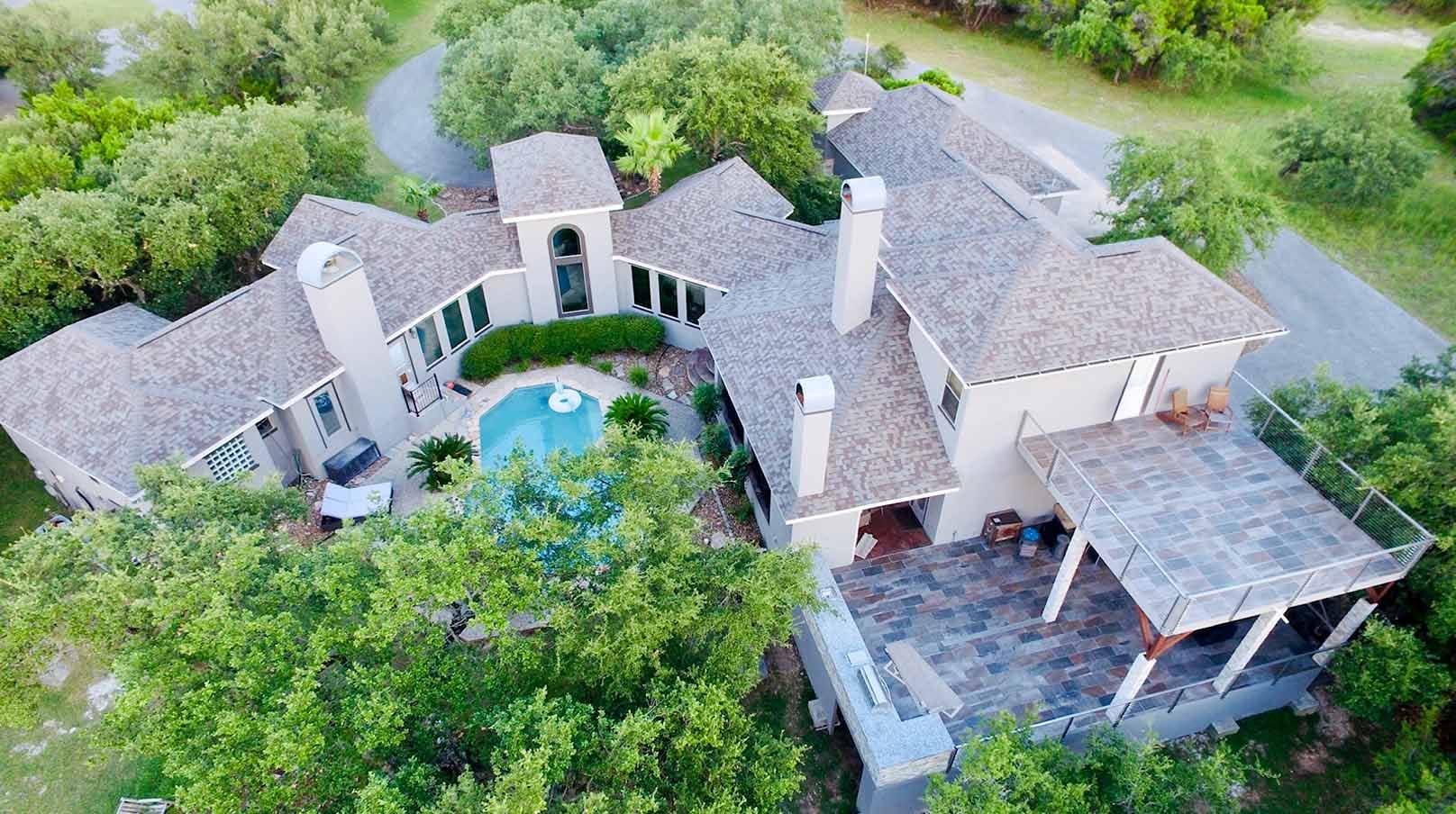 Aerial view of a large luxury home with a courtyard pool, tiled patio deck, and multiple chimneys