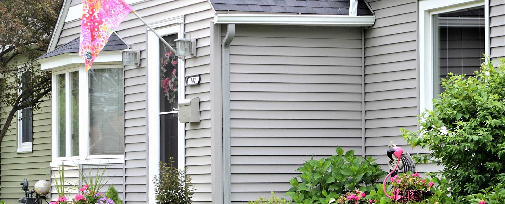 Home exterior with gray siding, a wreath on the front door, and landscaping with pink flowers
