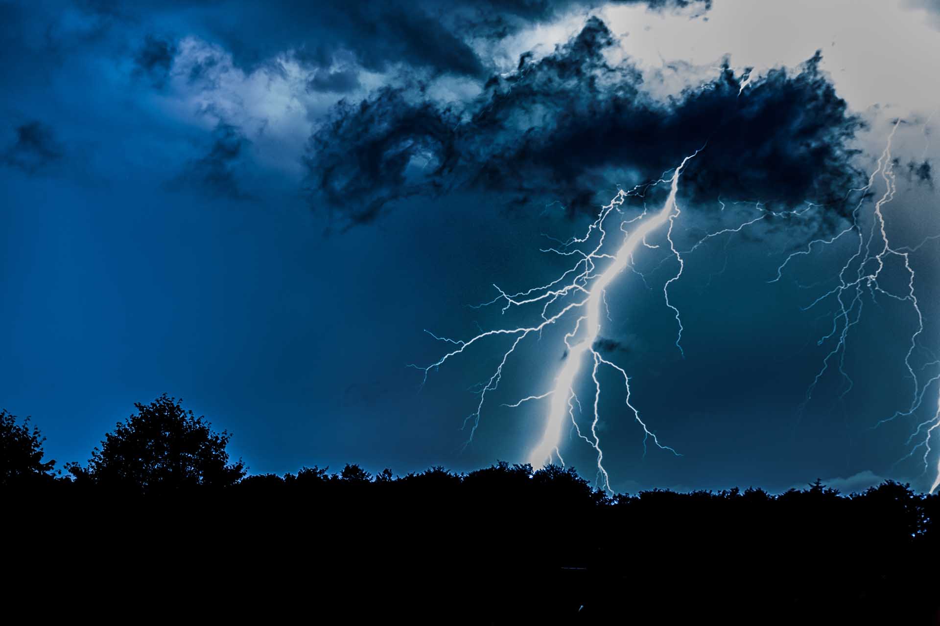 Lightning strikes from dark storm clouds over silhouetted trees during a Central Texas thunderstorm