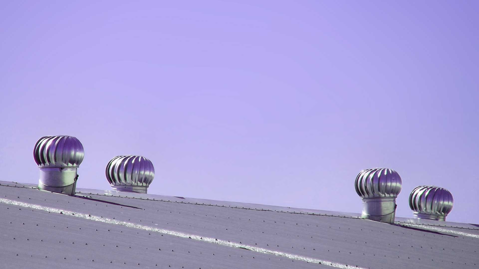 Four spinning turbine ventilators mounted on a metal roof against a purple-tinted sky